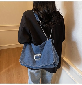 Detail of blue denim tote bag with silver metal buckle and chain link shoulder strap
