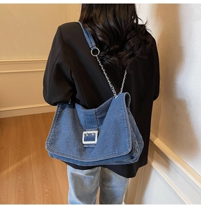 Detail view of denim shoulder bag with silver square buckle and metal chain strap on model