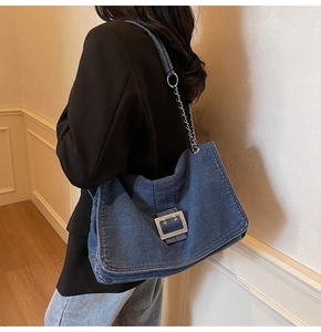 Detail of blue denim shoulder bag featuring a polished silver square buckle and chain strap