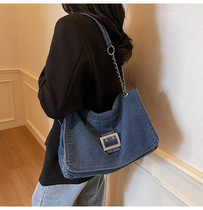 Detail of blue denim shoulder bag featuring silver metal buckle and chain strap on model