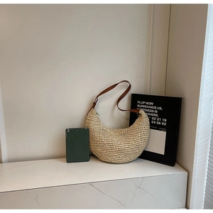 Summer beige woven crescent tote bag with brown leather strap on white minimalist desk