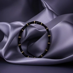Detail of black bamboo style bracelet with gold accents on elegant purple satin silk