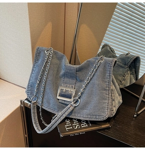 Detail of blue denim tote bag with silver metal buckle and woven chain shoulder strap
