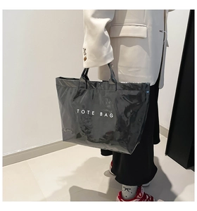Glossy black tote bag with white lettering held by a model in a minimalist setting
