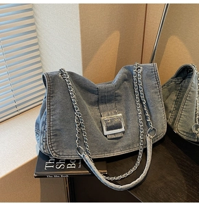 Detail of blue denim shoulder bag featuring silver chain strap and metal buckle