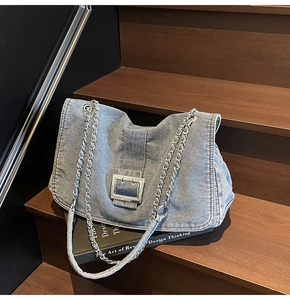Detail of light blue denim tote bag with silver buckle on a dark wooden step