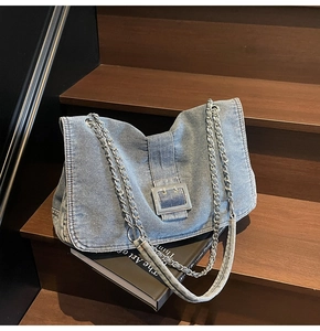 Detail of light blue washed denim tote bag featuring a silver square buckle and chain strap