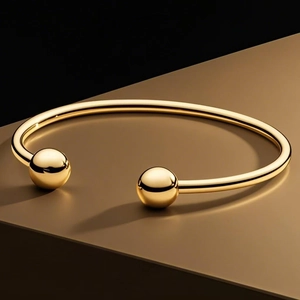 Minimalist gold titanium steel open bangle featuring polished metal spheres at each end