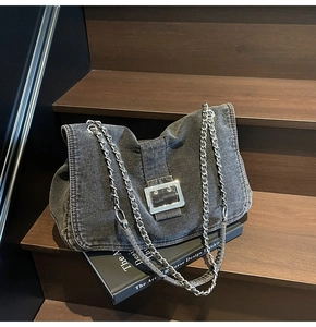 Detail of dark denim underarm bag with silver chain and large polished metal buckle