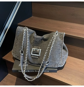 Detailed close-up of dark grey denim shoulder bag with a silver buckle on wooden stairs