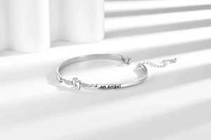 Detail eines silbernen Engelsflügel-Armbands mit Fußabdruck und 'an Angel' Gravur