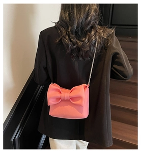 Detail of pink bow-shaped crossbody bag featuring delicate texture and silver chain strap