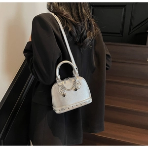 Dettaglio borsa a conchiglia argento con rivetti e catena su blazer nero elegante
