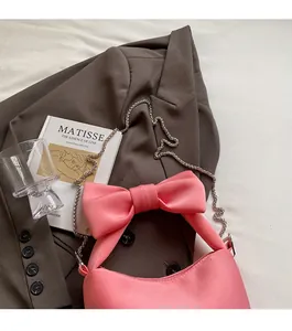 Pink satin bow handbag with silver chain strap placed on a brown suit jacket