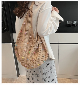 Detailed view of handmade woven straw shoulder bag with colorful pearl accents on a model