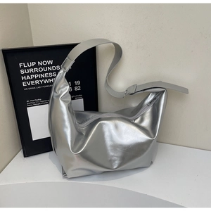 Gros plan du sac hobo argenté brillant avec large bandoulière sur un socle minimaliste