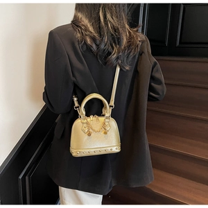 Dettaglio borsa a conchiglia oro champagne con texture metallica, borchie e ciondolo B