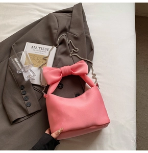 Detail of pink satin pillow bag featuring a large bow handle and silver chain strap