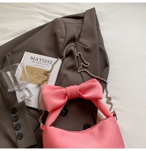 Detail of a pink satin handbag featuring a large decorative bow and a silver metal chain