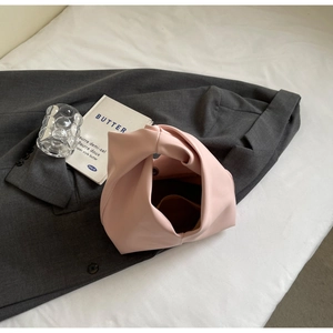 Top view of a pale pink knotted handbag on a grey suit jacket with lifestyle props