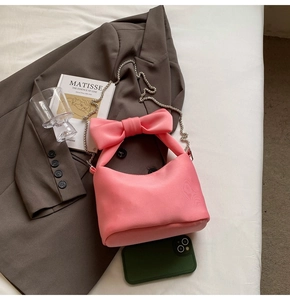 Detail of pink satin bow shoulder bag with fine metal chain on minimalist background