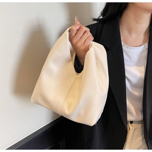 Close-up of beige minimalist trapezoid handbag styled with a classic black office blazer