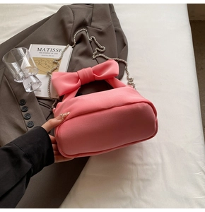 Detail of pink nylon pillow bag featuring a large satin bow handle and silver chain strap