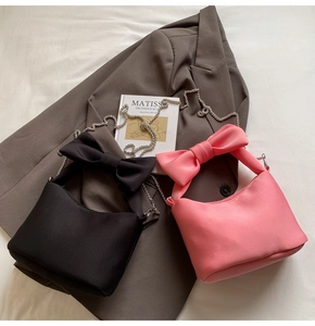 Detail of trendy bow handbags in black and pink with metal chains on soft fabric