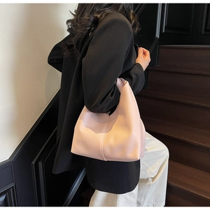 Close-up of a light pink minimalist hobo bag styled with a dark blazer in a studio setting