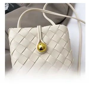Detail show of off-white woven crossbody bag with gold bead accent and leather texture