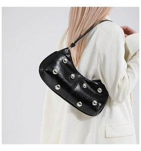 Détail du sac sous l'aisselle en cuir verni noir avec clous argentés sur blazer blanc