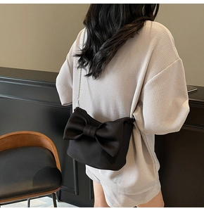 Detail of black nylon crossbody bag with large 3D bow decoration and silver chain strap