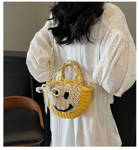 Detail of hand-woven straw bag with black smiley face, pearl charm, and lace decoration