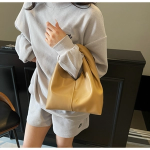 Close-up of beige cloud handbag with soft leather pleats held by model in casual set