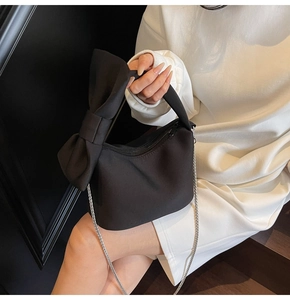 Detail of a black nylon chain bag featuring a large decorative bow and silver strap