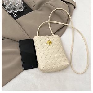 Detail of off-white woven phone bag with gold spherical clasp and long shoulder strap