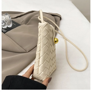 Detailed close-up of woven cream leather phone bag featuring a gold spherical clasp