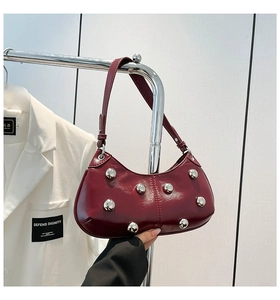 Gros plan sur le sac porté épaule en cuir verni bordeaux avec de gros clous métalliques