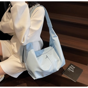 Détail du sac hobo en cuir verni bleu clair brillant avec poche zippée sur un escalier