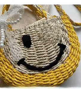 Close-up of yellow straw bag featuring a black woven smiley face and pearl bead strap