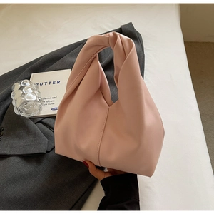 Detailed view of pink leather hobo bag with a knot handle placed on a gray suit jacket
