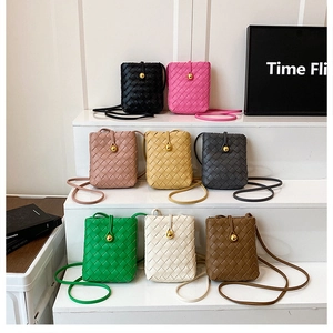 Multiple colors of woven crossbody phone bags displayed on a clean white stepped stand