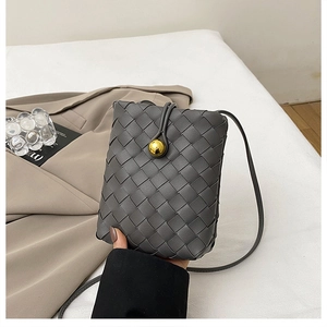 Detail view of grey woven leather texture and gold spherical clasp on a mini crossbody bag