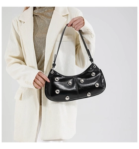 Détail d'un sac lune noir brillant à rivets argentés porté avec un blazer blanc