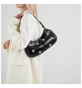 Détail d'un sac porté épaule en cuir verni noir avec clous argentés sur blazer ivoire