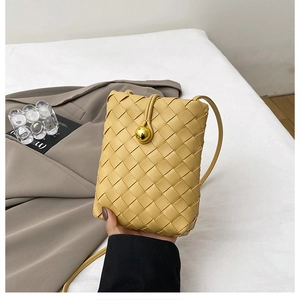 Detail of a woven ginger yellow crossbody phone bag with a large gold ball buckle