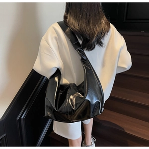 Vue arrière d'un sac hobo noir brillant avec large bandoulière porté par un mannequin