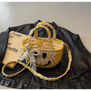 Detailed macro view of yellow straw woven bag featuring smiley embroidery and pearl bow