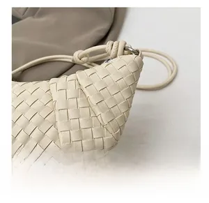 Detail view of beige hand-woven dumpling bag showing premium texture and metallic rings