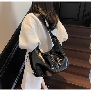 Sac hobo noir brillant avec large bandoulière, porté par un mannequin en extérieur